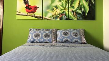 Una cama con ropa de cama estampada, una pared con un cuadro de un pájaro y una pared verde.