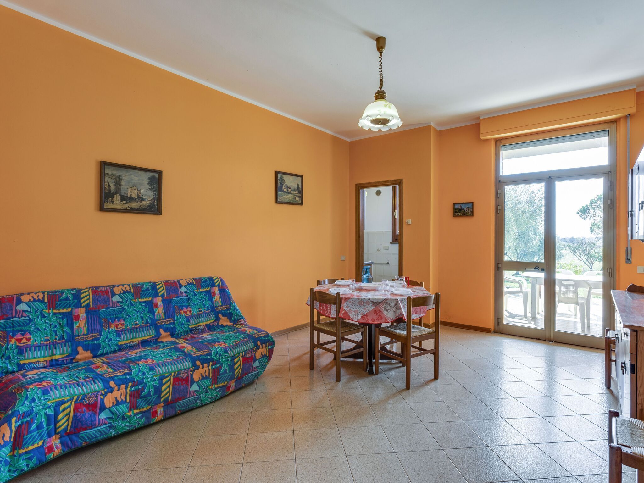 Una habitación con un sofá colorido, una mesa de comedor con sillas y un ventanal grande.