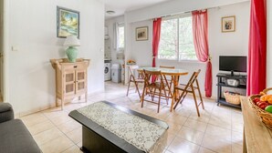 A living room with a sofa, a coffee table, a dining table with chairs, a TV, and a kitchen area with a washing machine. - Mougins Hideaway for 4 Guests (Mougins)
