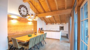 A dining area with a wooden table and chairs, a kitchen with white cabinets, and a clock on the wall. - Luxury penthouse in Brixen im Thale (Brixen im Thale)