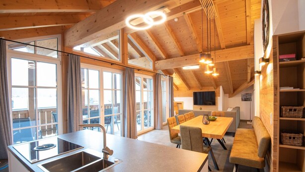 A modern kitchen with a central island, a dining area with a table and chairs, and a cozy seating area with a bench. - Luxury penthouse in Brixen im Thale (Brixen im Thale)