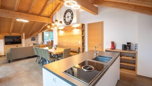 A modern kitchen with a central island, wooden beams, and a large clock on the wall. - Luxury penthouse in Brixen im Thale (Brixen im Thale)