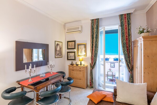 A room with a dining table, chairs, a wooden cabinet, a mirror, and a view of the sea through a sliding glass door.