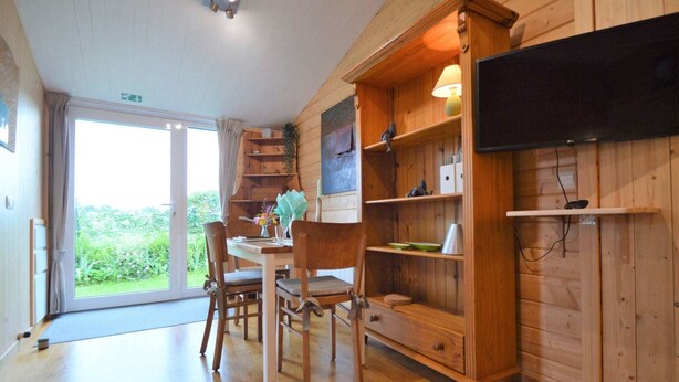 Un intérieur en bois comprenant un coin repas, un téléviseur fixé au mur et une vue sur la verdure à l’extérieur.