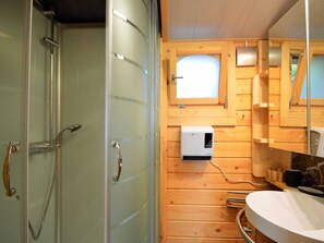 A wooden cabin bathroom with a glass shower enclosure, a window, and a built-in sink.