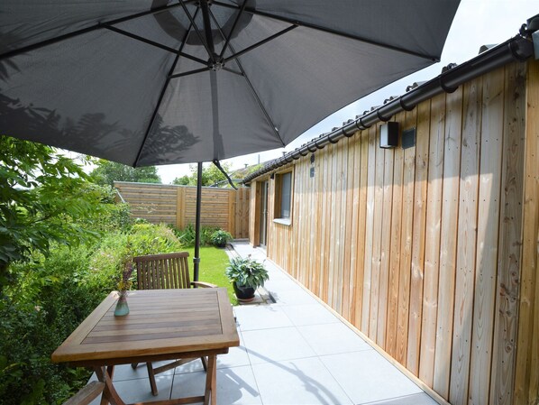 A wooden deck with a table and an umbrella, surrounded by a wooden fence and greenery.