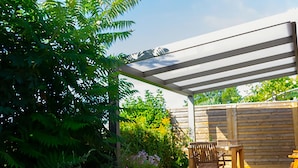 Un patio couvert, agrémenté de chaises et d’une table en bois, entouré d’une végétation luxuriante et d’une clôture en bois.