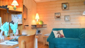 Un intérieur chaleureux avec des éléments en bois, un canapé de couleur turquoise, des murs en bois et un coin repas avec une table mise pour deux personnes.