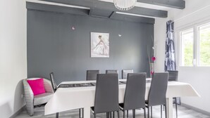A modern dining area with a white table and grey chairs, a grey accent wall, and a pendant light.