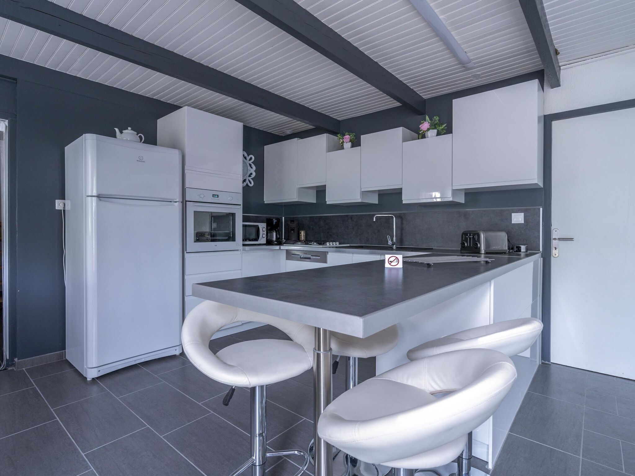 A modern kitchen with a central island, white bar stools, a refrigerator, an oven, a microwave, and a coffee maker.