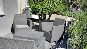 A patio area with wicker furniture, including a sofa and chairs, surrounded by greenery and a tree.