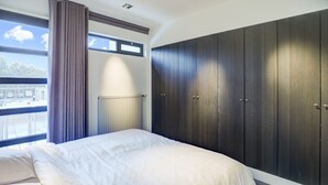 Ein Schlafzimmer mit einem großen Bett, einem Fenster mit Vorhängen, einem Heizkörper und dunklen Holzschränken.