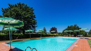 A rectangular swimming pool with a brick border, surrounded by green umbrellas and lounge chairs.