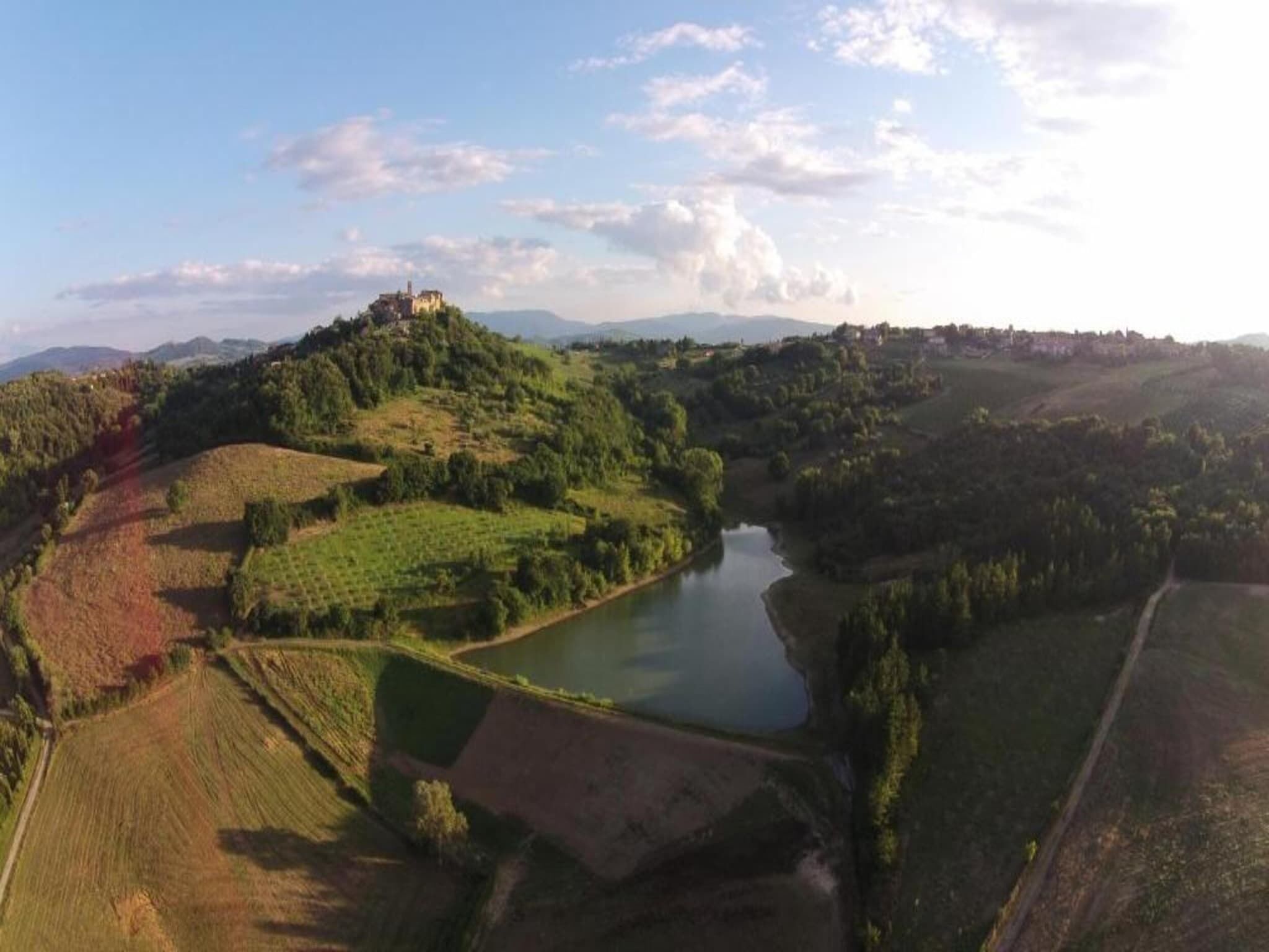 Vista panorámica de un paisaje montañoso con un edificio pequeño en una colina, rodeado de campos y un río.