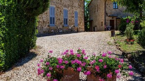 Un edificio de piedra con camino de grava y un jardín lleno de flores rosadas.