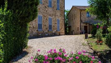 A stone building with a gravel driveway and a garden with pink flowers.