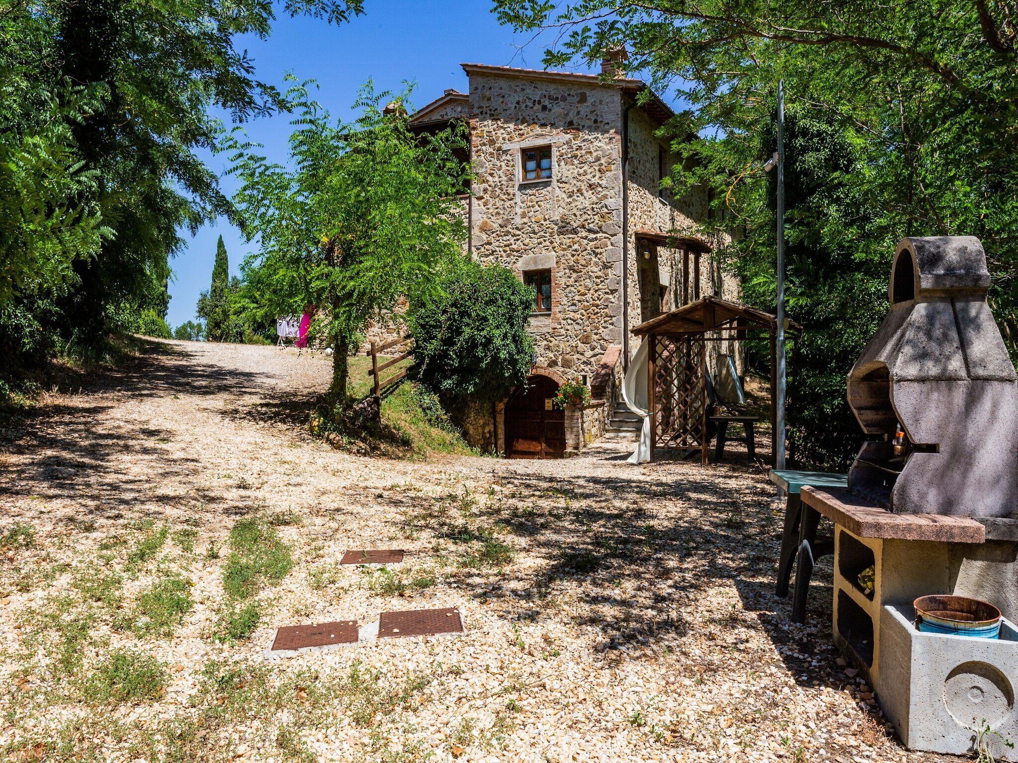 A stone building with a rustic appearance, a gravel path leading to it, and a chimney-like structure to the right.