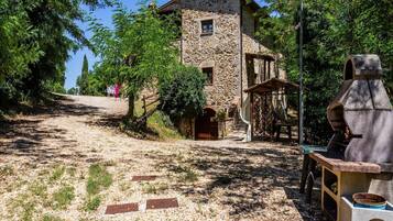 A stone building with a rustic appearance, a gravel path leading to it, and a chimney-like structure to the right.