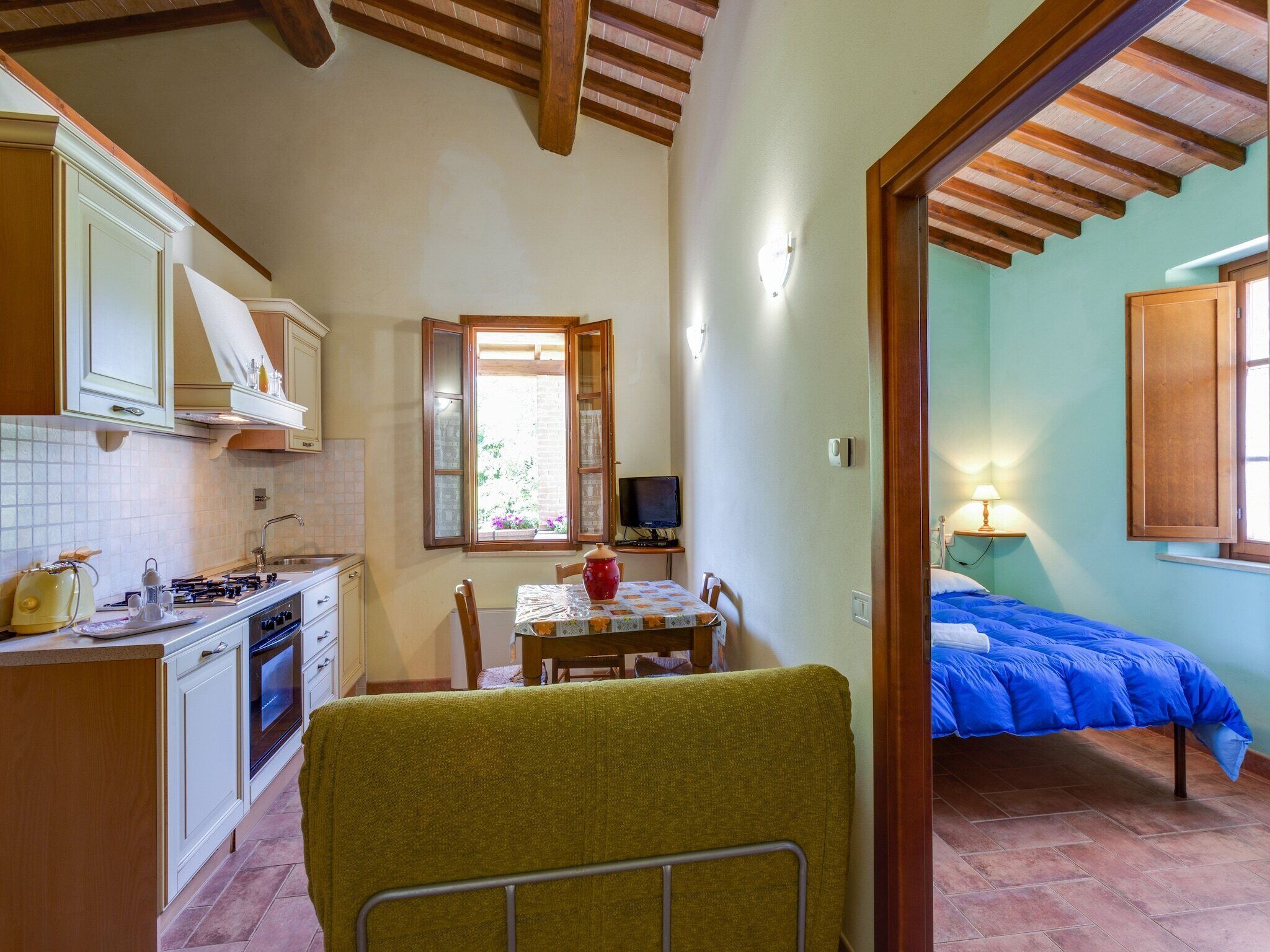 A compact kitchen with a dining area, a small TV, and a bedroom with a blue bedspread.