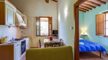 A compact kitchen with a dining area, a small TV, and a bedroom with a blue bedspread.