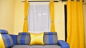 Uma sala de estar com sofá seccional, cortinas amarelas e janela com cortinas brancas finas.