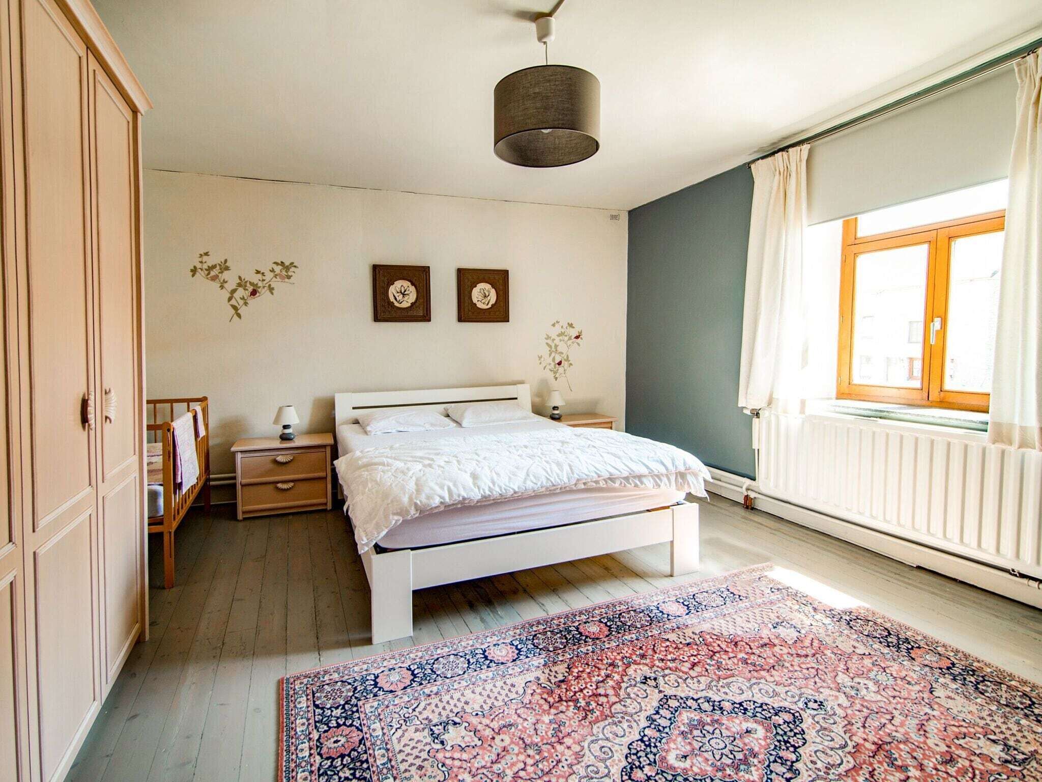 Een slaapkamer met een bed, nachtkastjes, een kaptafel, een raam met gordijnen en een radiator.