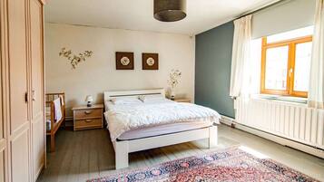 Een slaapkamer met een bed, nachtkastjes, een kaptafel, een raam met gordijnen en een radiator.