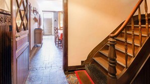 Un pasillo con escalera de madera, piso estampado y una puerta que da a otra habitación.