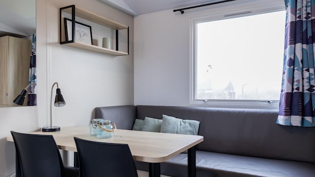 Una habitación moderna con una mesa de comedor, sillas, un sofá, una ventana con cortinas y un estante con fotografías enmarcadas.