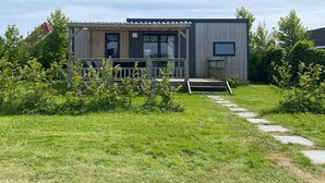 A modern, single-story cabin with a wooden deck, large windows, and a small porch.