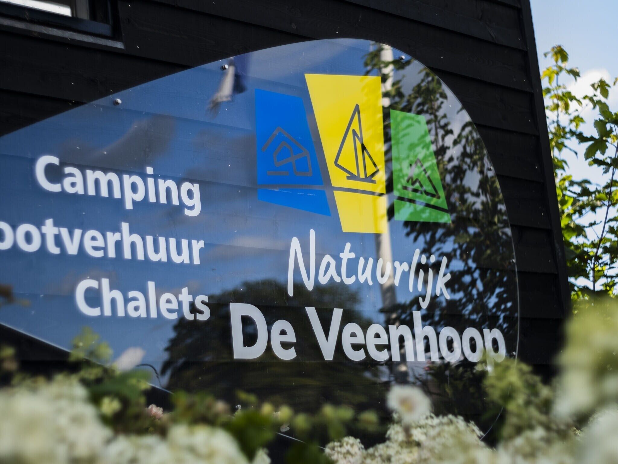 Señal con el texto 'Camping, Bootverhuur, Chalets, Natuurlijke De Veenhoek' que indica un lugar de camping y alquileres.
