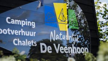 Señal con el texto 'Camping, Bootverhuur, Chalets, Natuurlijke De Veenhoek' que indica un lugar de camping y alquileres.