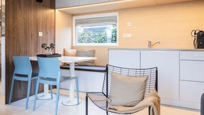 A modern kitchen with a dining area, featuring a wooden accent wall, a window with a view, and a coffee machine.
