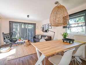 A modern living room with a wooden dining table, white chairs, a grey sofa, and a wicker hanging light fixture. - Modern chalet in Voorthuizen near the forest (Voorthuizen)