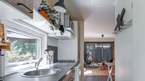 A modern kitchen with a large window, stainless steel sink, and a dining area with a table and chairs. - Modern chalet in Voorthuizen near the forest (Voorthuizen)