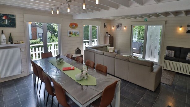 A dining area with a table and chairs, a sofa, and a kitchen area with a radiator. - Stylish Chalet with Room (Durbuy)