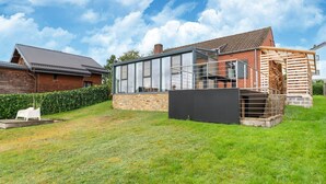 Una casa moderna con una amplia extensión de vidrio, un cimiento de piedra y una terraza de madera.