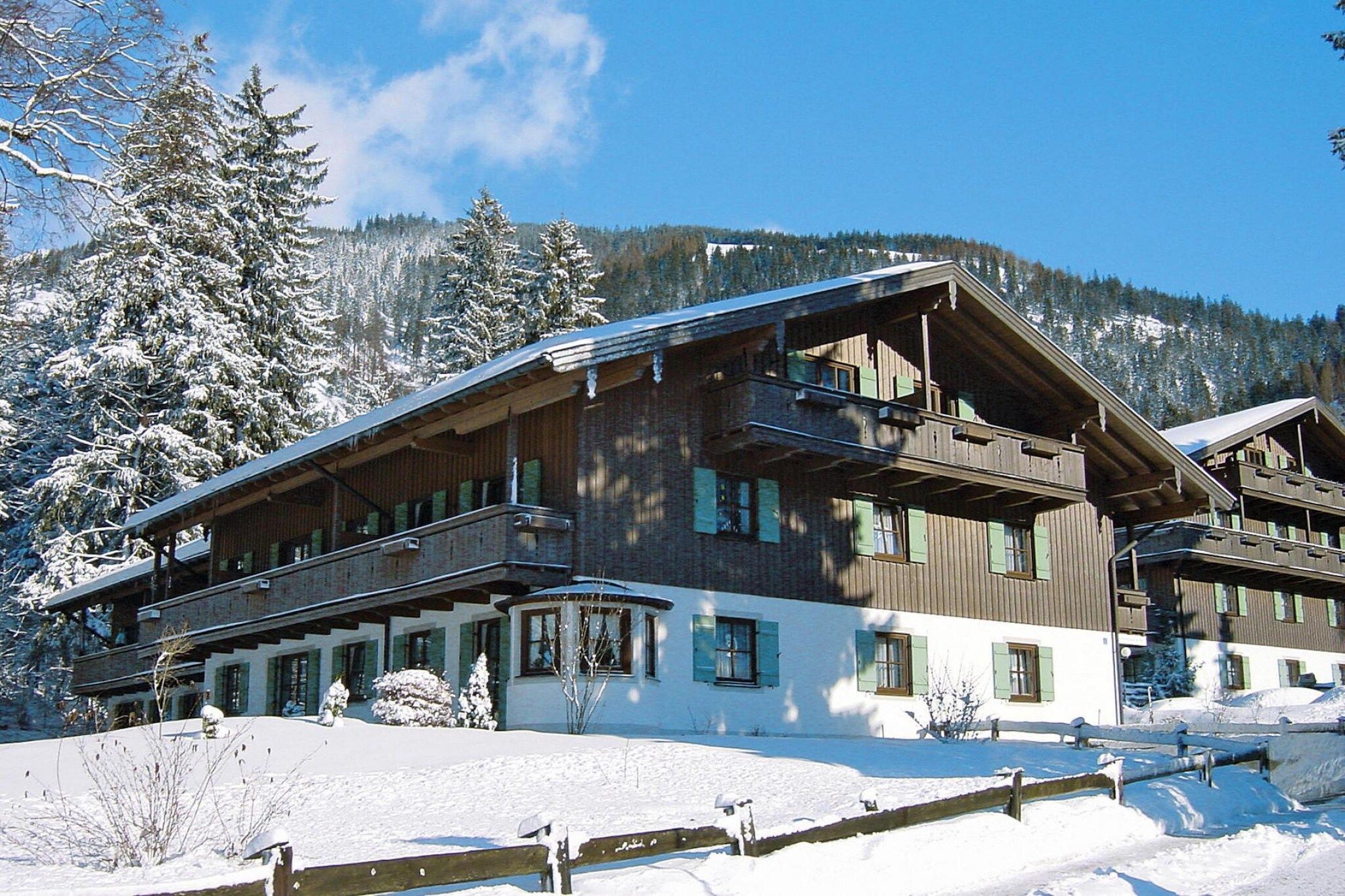 Un edificio de madera de varios pisos con balcones, rodeado de árboles y montañas cubiertas de nieve.