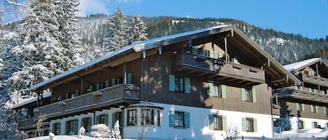 Un edificio de madera de varios pisos con balcones, rodeado de árboles y montañas cubiertas de nieve.