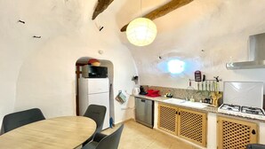Een compacte keuken met een eethoek, met een houten tafel, stoelen, een inbouwfornuis en een hangende lamp.