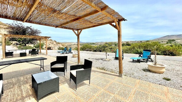 Een terras buiten met rieten meubilair, een pergola en uitzicht op het landschap.