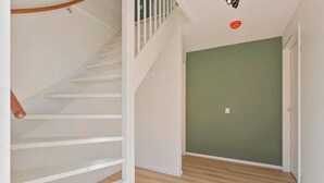 Una escalera con barandillas blancas que lleva a una habitación con pared verde y suelo de madera.