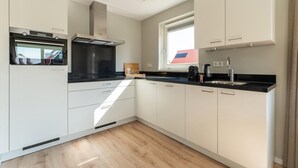 Una cocina moderna con gabinetes blancos, una encimera negra y una ventana con vistas a un edificio de tejados rojos.