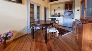 A dining area with a wooden table and chairs, a kitchen with a stove and cabinets, and a wooden ceiling. - Farmhouse in Tuscany with Pool near Montecastello (Toscana)