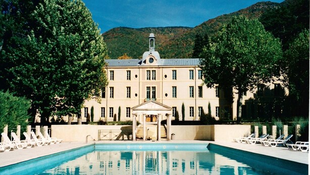 Un grande edificio con piscina, circondato da alberi e colline.