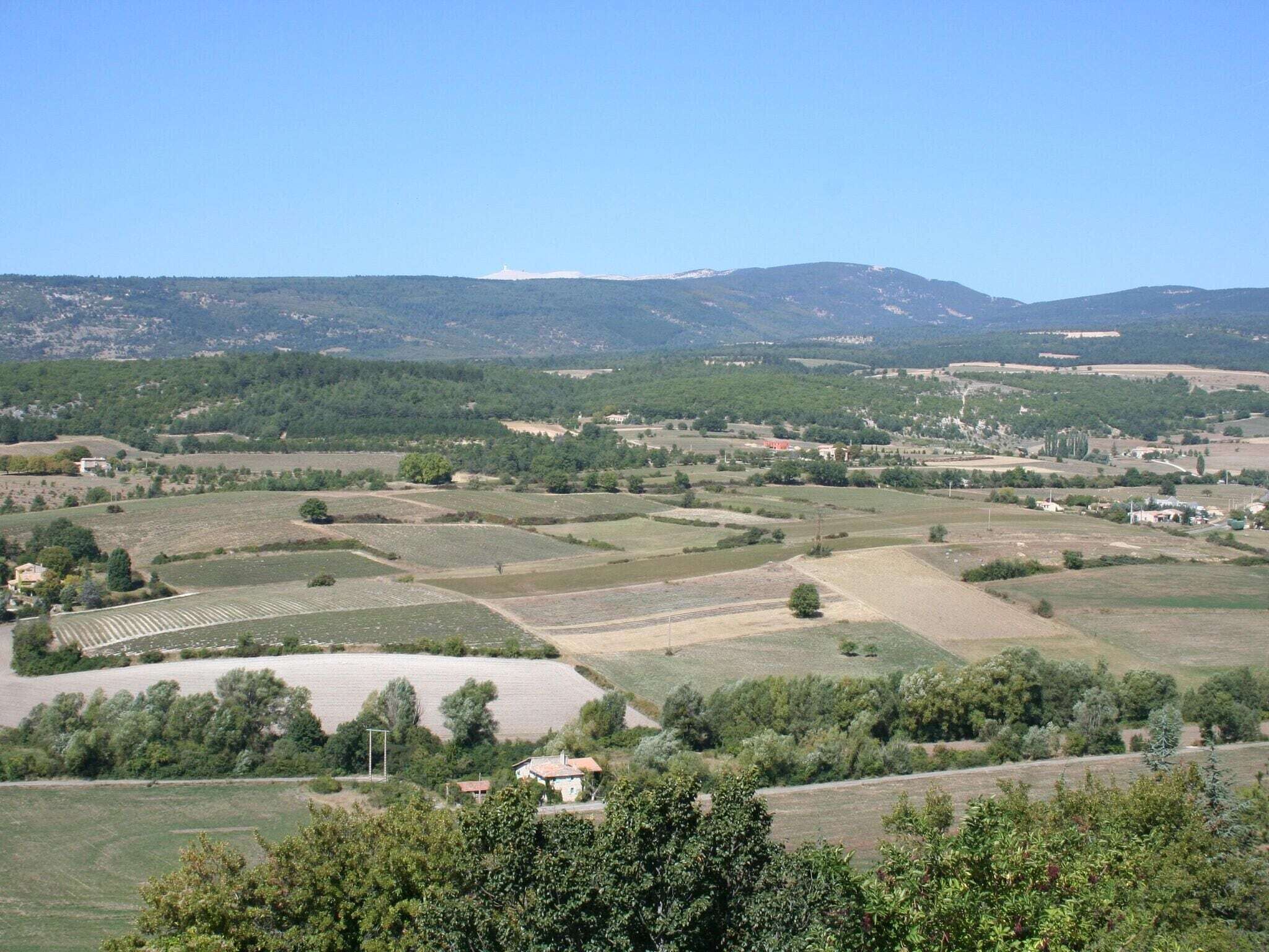 Un paysage rural avec des champs, des maisons éparpillées et des collines en arrière-plan.