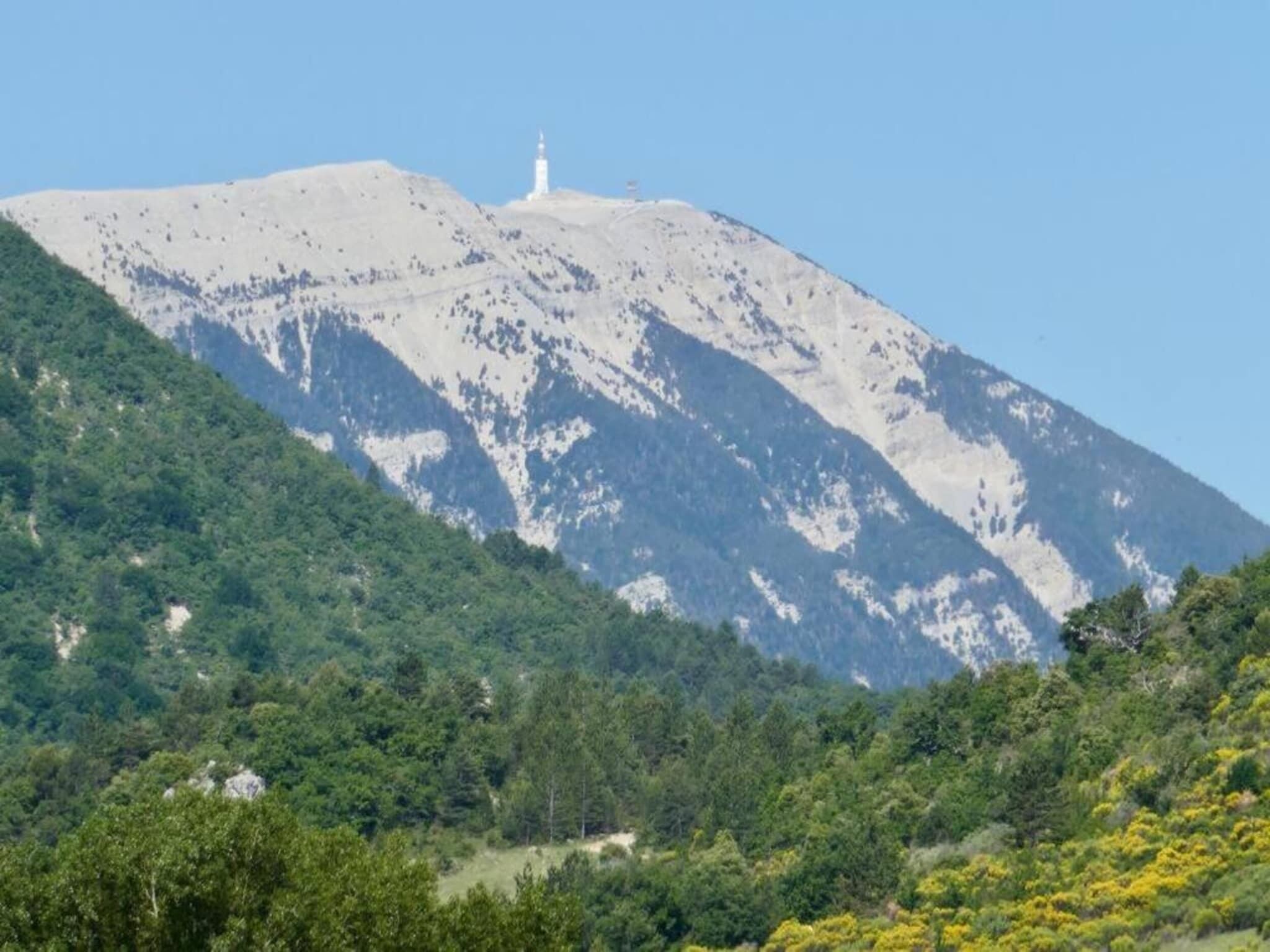 Una montaña con un faro en la cima, rodeada de un bosque verde y tupido.