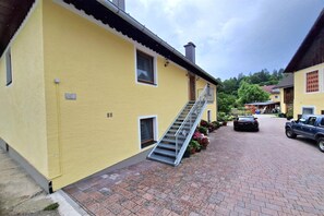 A yellow building with a staircase leading to a door, a parked car, and a brick pathway.