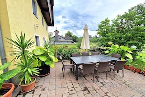 Um pátio com mesa e cadeiras, rodeado por plantas em vasos e um edifício amarelo ao fundo.