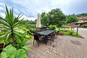 An outdoor patio with a brick floor, a table with chairs, and potted plants.